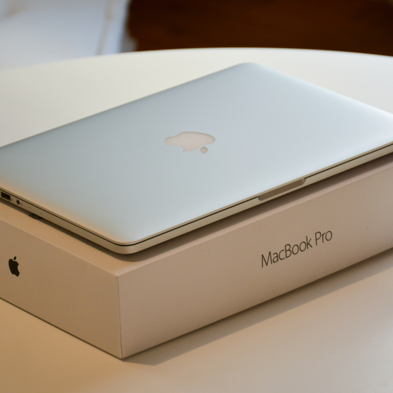 A closed Silver Macbook Pro with apple logo visable on top of a MacBook pro box on top of a white table